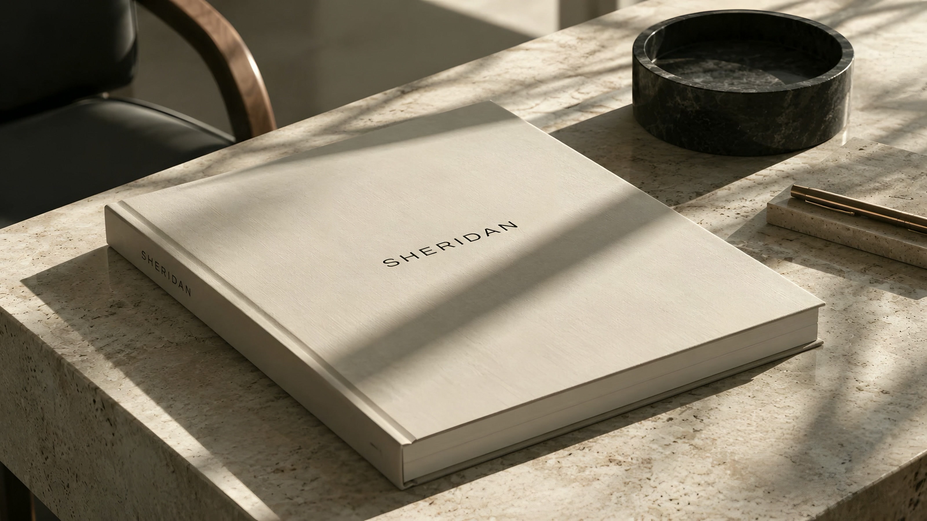 A linen-bound Sheridan book on a travertine desk in afternoon light