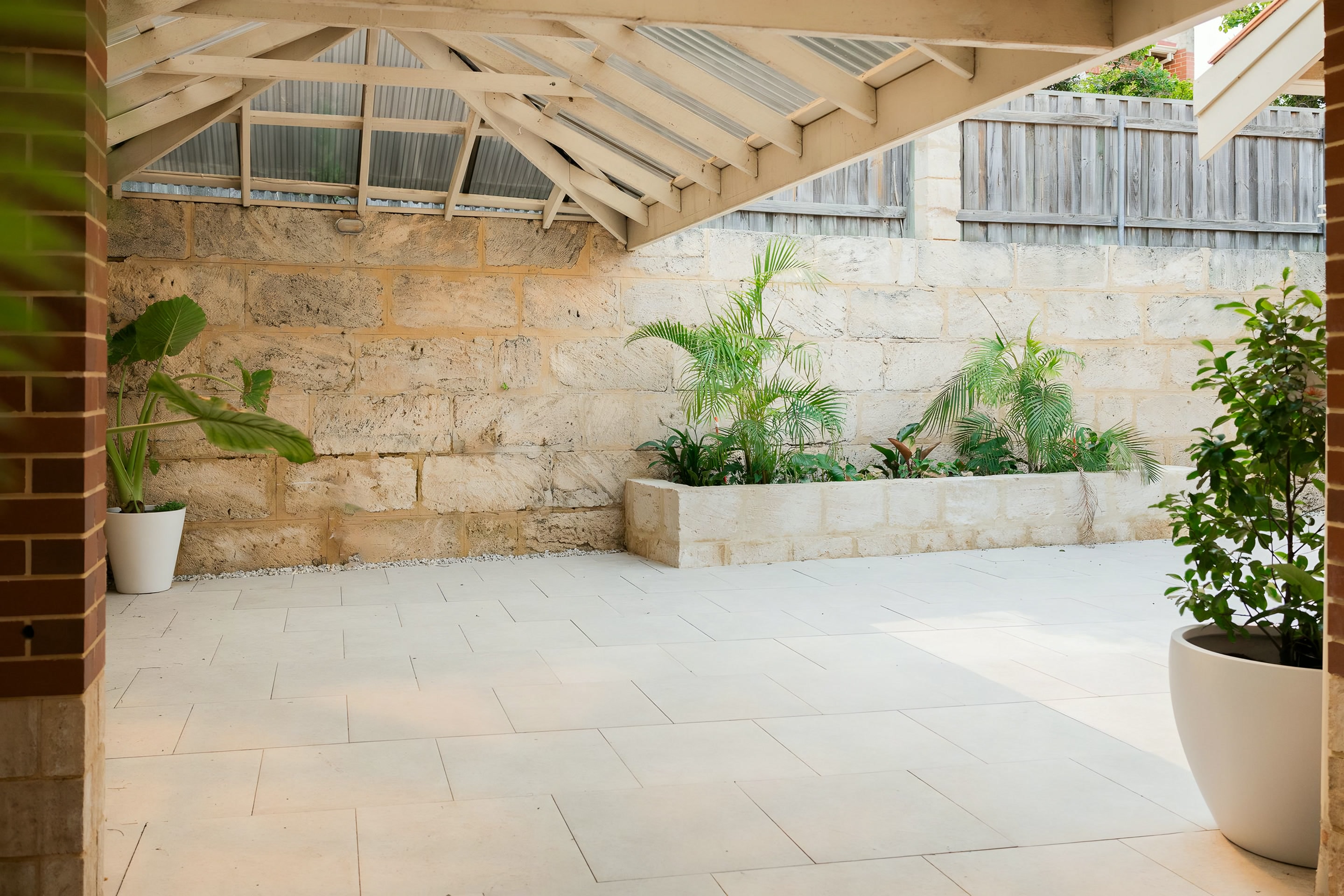 A paved courtyard with a limestone planter under a pergola