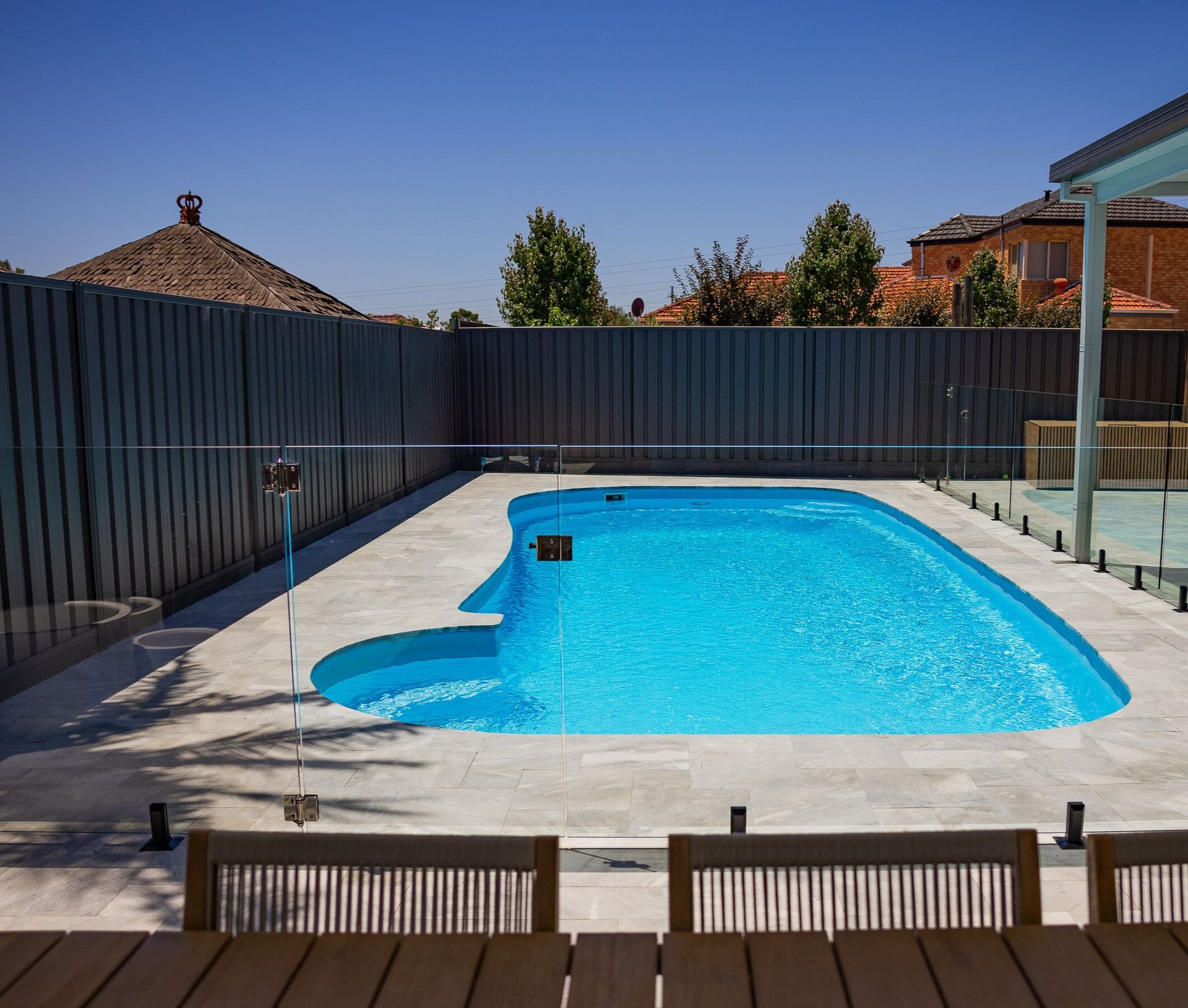 A curved pool in stone paving behind a glass fence