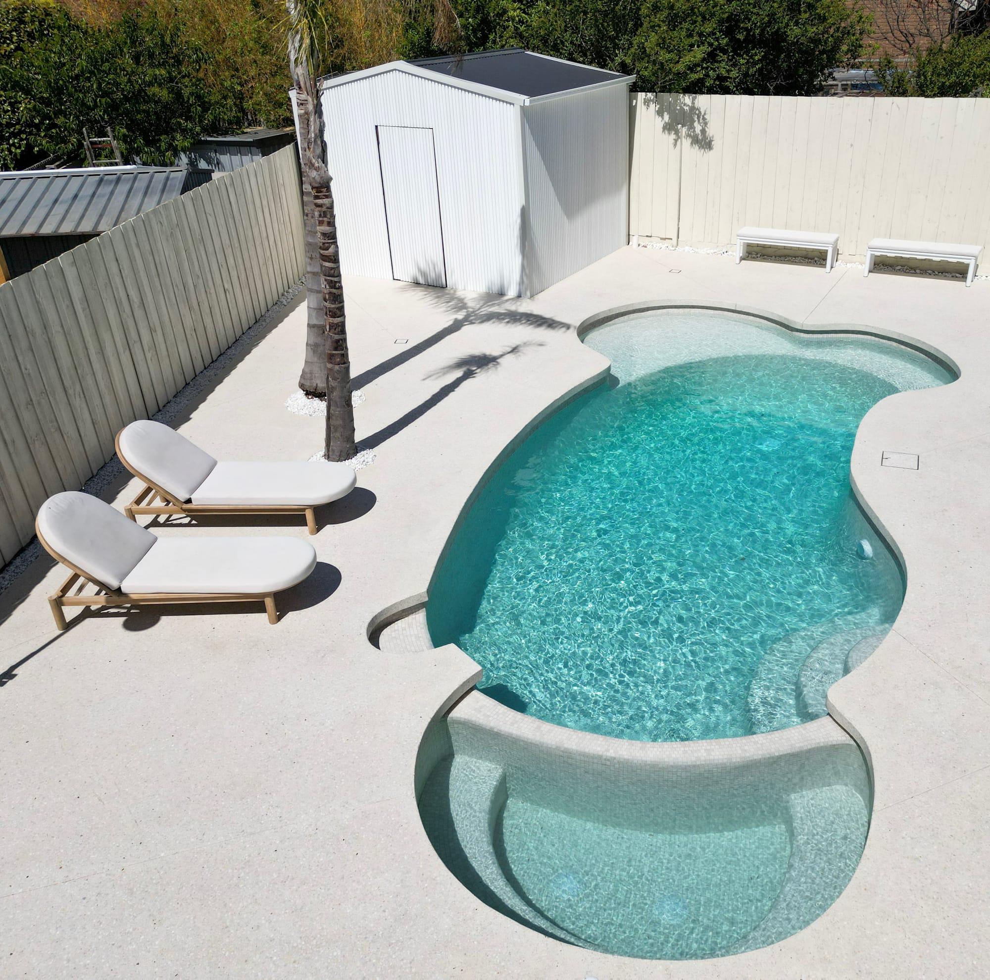 A curved pool with built-in steps and a pale stone surround
