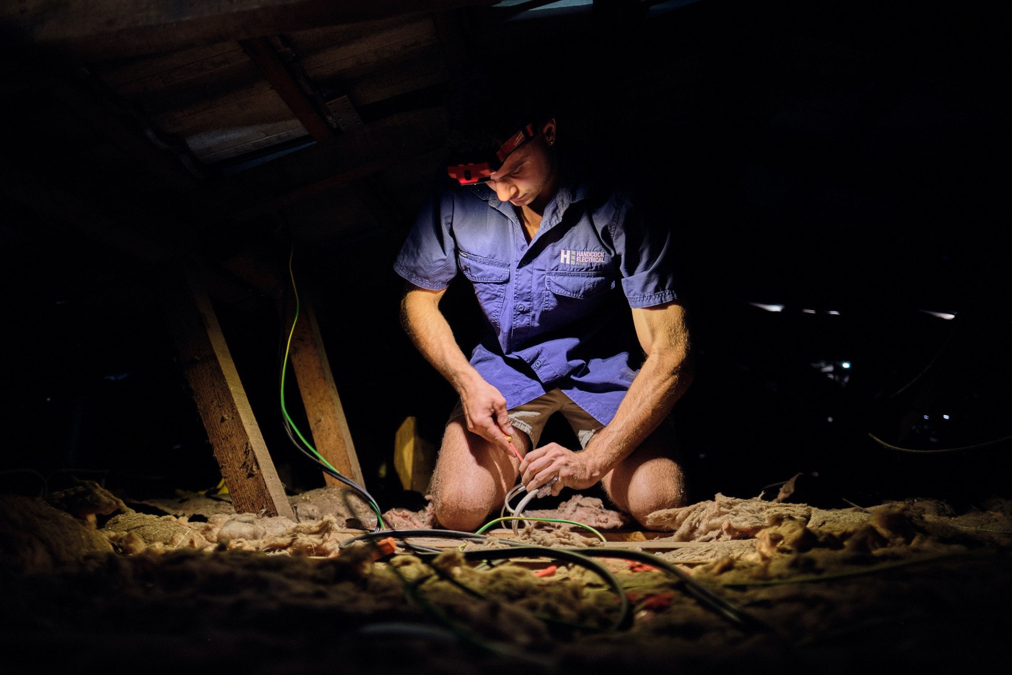 An electrician working in a roof space by headlamp
