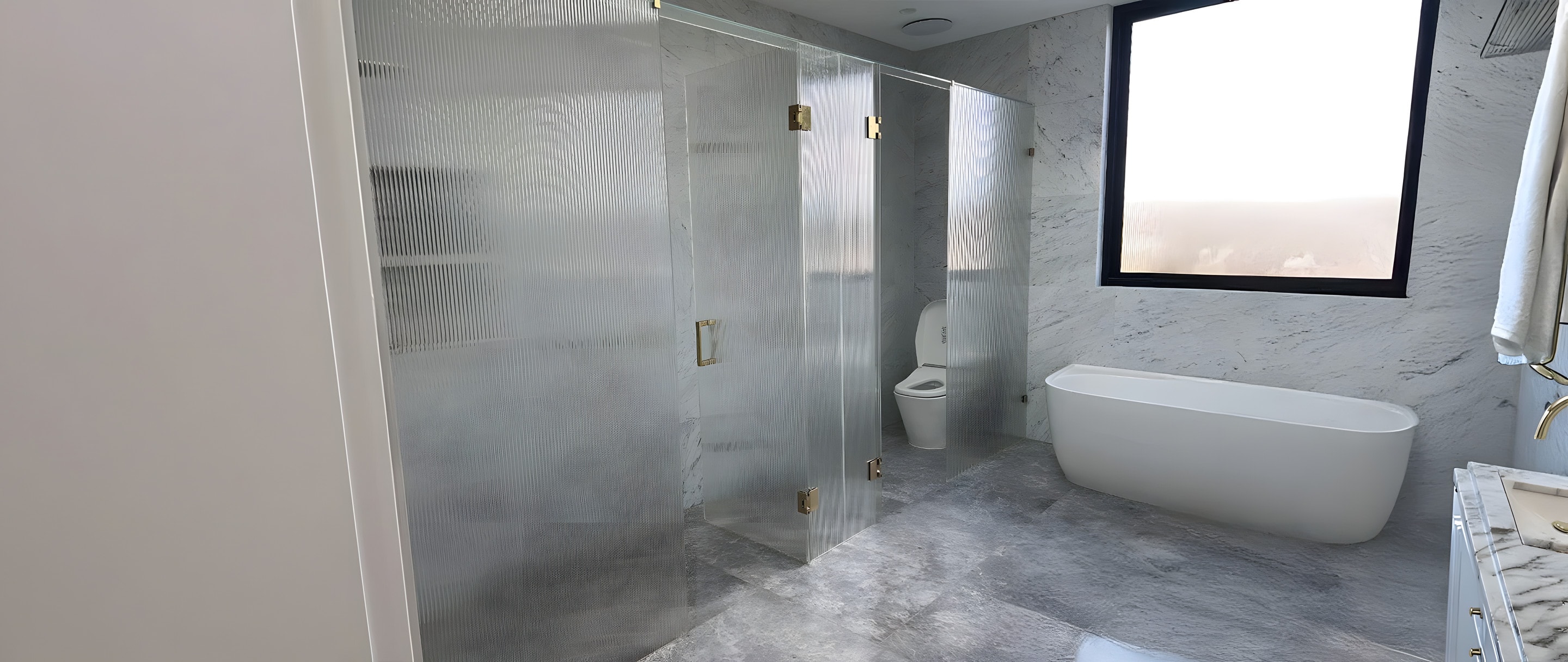 Fluted-glass shower and toilet enclosures with brass hardware in a marble bathroom